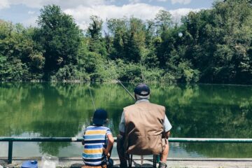 man in black shirt sitting on chair near lake during daytime